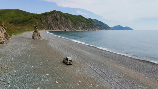 A solitary SUV travels along a rugged beach in Primorsky Krai, Russia, showcasing adventure and natural beauty.